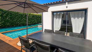 Een zwembadterras met een tafel, stoelen en een grote parasol, met uitzicht op een zwembad.