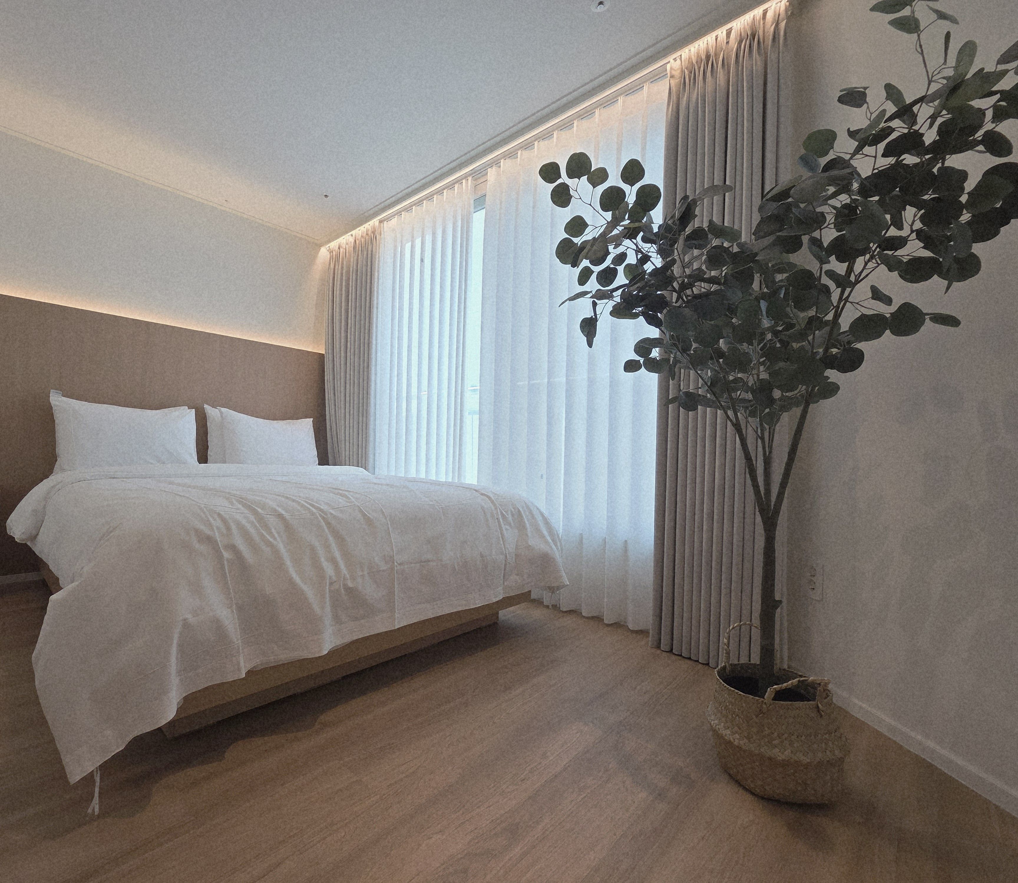 Une chambre à coucher avec un lit, des rideaux, une plante en pot et un panier en osier.