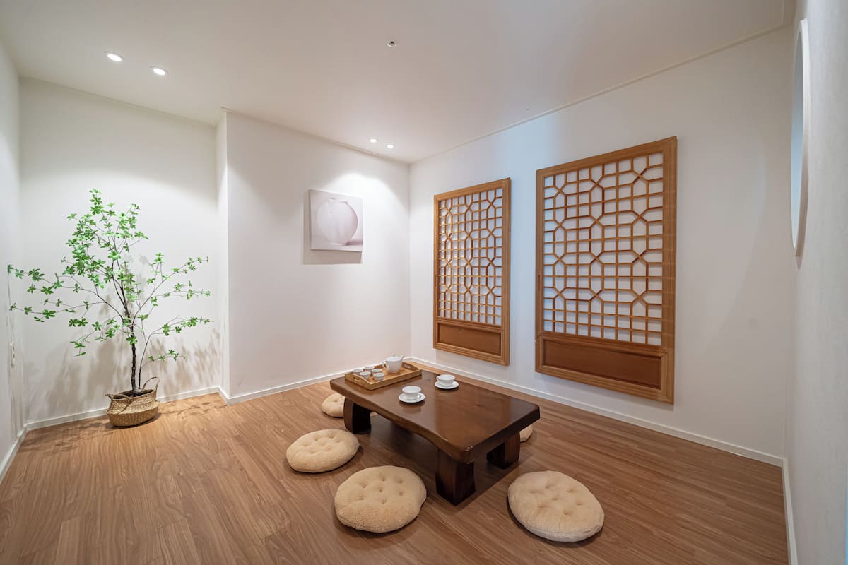 A room with a wooden floor, a table with stools, a potted plant, and traditional wooden screens.