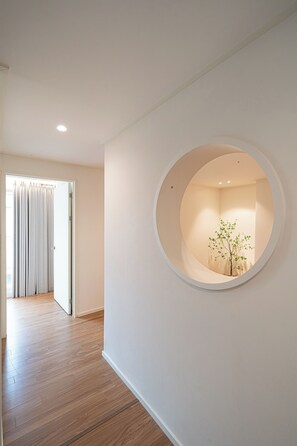 Un pasillo con piso de madera, una pared blanca con un ventanal circular y una puerta con cortinas.