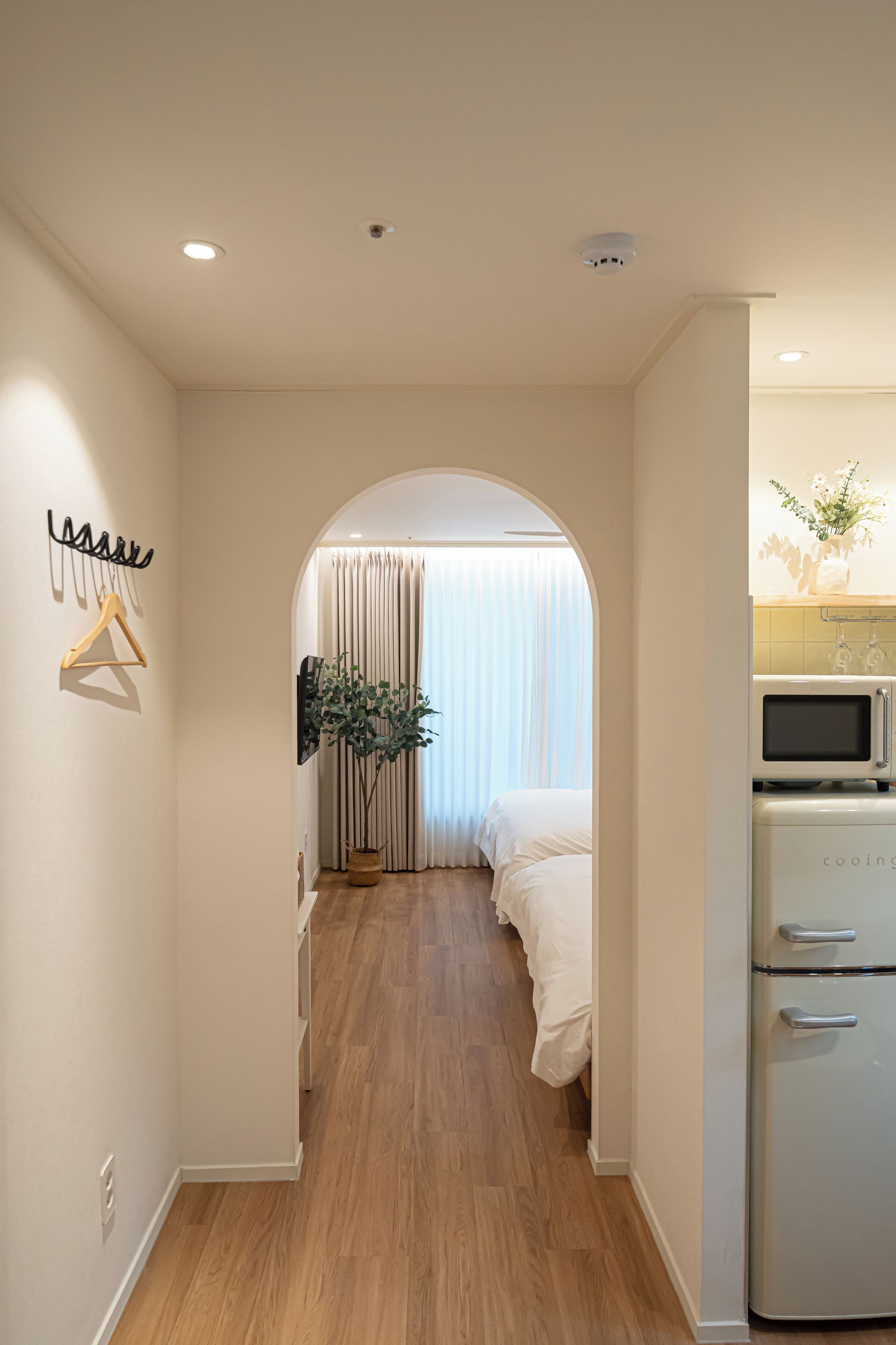A hotel room with a wooden floor, a bed with white bedding, a microwave, and a small potted plant.