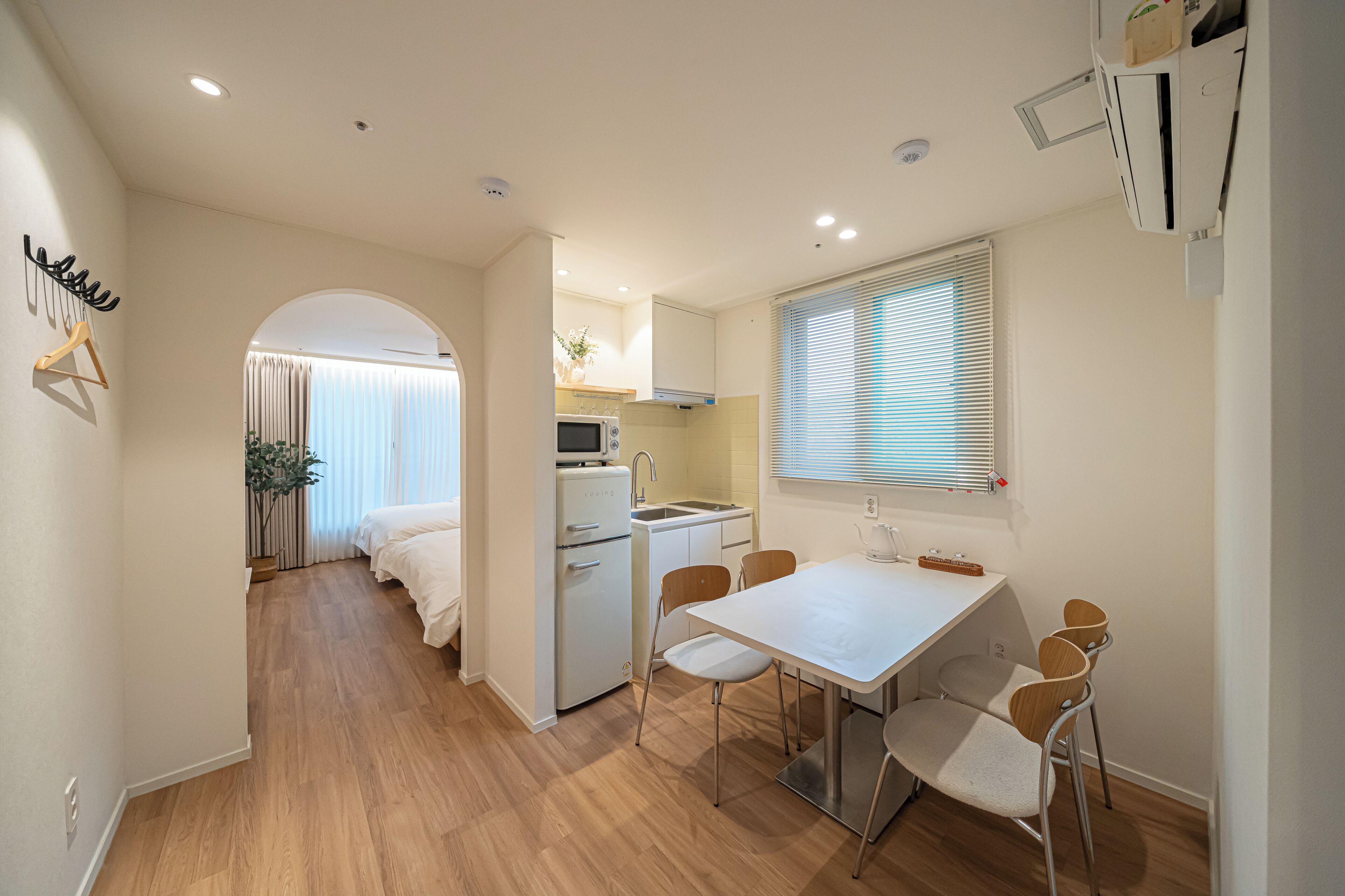 A compact kitchen with a dining area, a small refrigerator, and a window with blinds.
