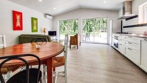 A modern kitchen with white cabinets, a dining area with a wooden table, and a view of greenery through the glass doors. - Luxueuse Villa avec piscine (Saint-Laurent-de-la-Pr)
