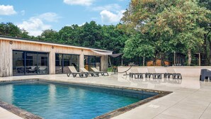 A swimming pool with lounge chairs, a wooden building with glass doors, and a covered patio area. - Luxueuse Villa avec piscine (Saint-Laurent-de-la-Pr)