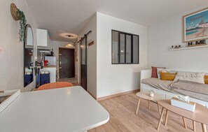 A compact living space with a kitchenette, a dining area, and a sofa with decorative pillows. - Appartement proche plage (Royan)