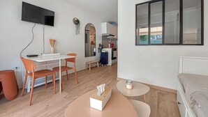 Un ambiente compatto con angolo cottura, un'area pranzo con due sedie, un piccolo tavolo rotondo e un divano.