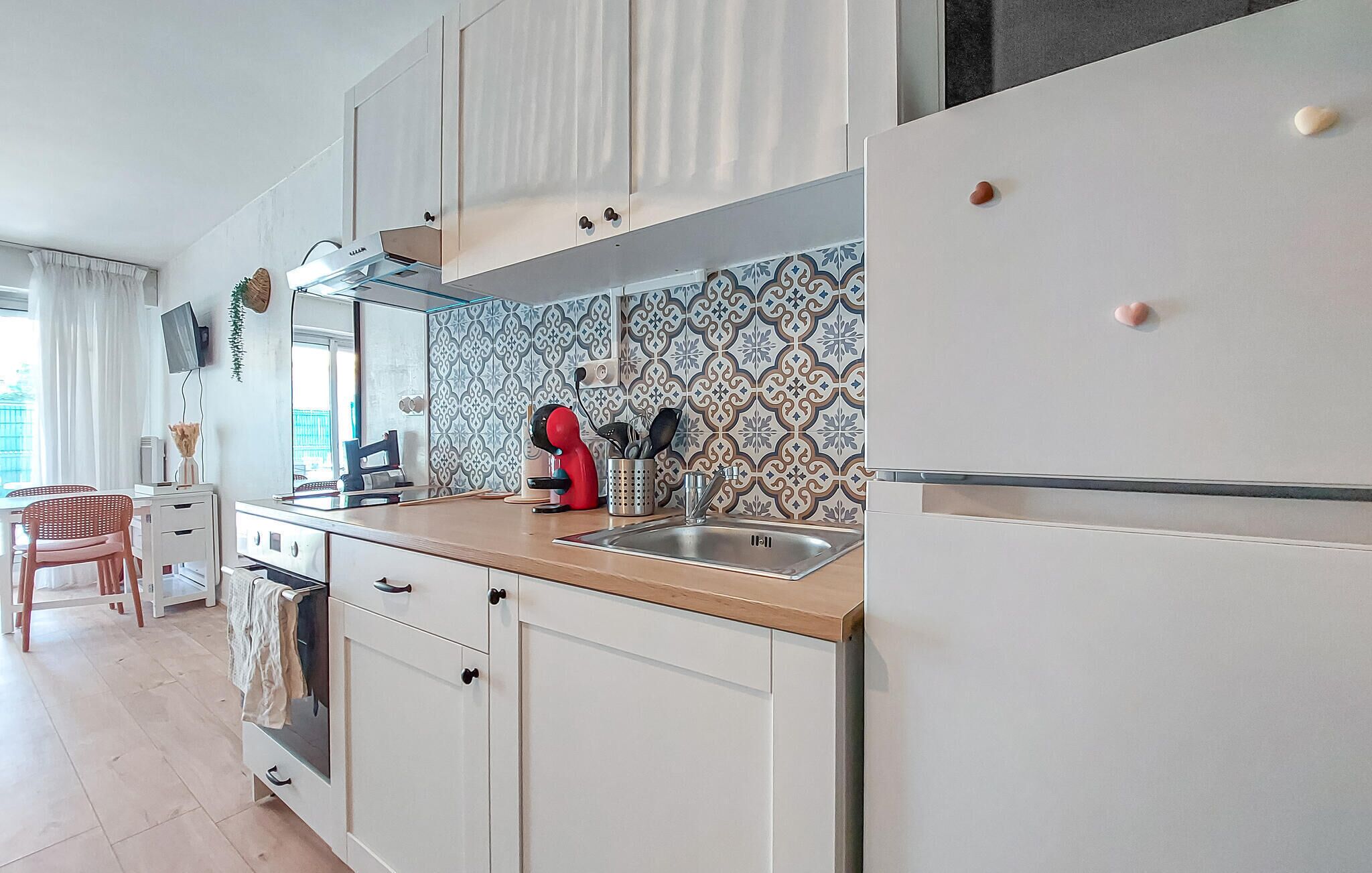 A modern kitchen with white cabinets, a stainless steel sink, and a red coffee machine.