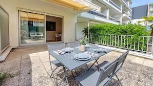 Area esterna con tavolo apparecchiato per quattro persone, una porta scorrevole in vetro e un balcone con ringhiera in metallo.