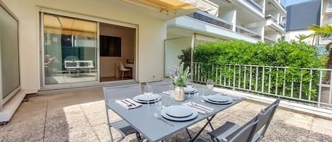 Un área de comedor al aire libre con una mesa preparada para cuatro, una puerta corrediza de vidrio y un balcón con barandilla de metal.