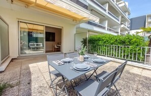 An outdoor dining area with a table set for four, a sliding glass door, and a balcony with a metal railing. - Appartement proche plage (Royan)