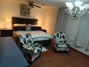 A bedroom with a bed, two chairs, a nightstand, a ceiling fan, and a chandelier. - Via Alejandro  (Tecate)