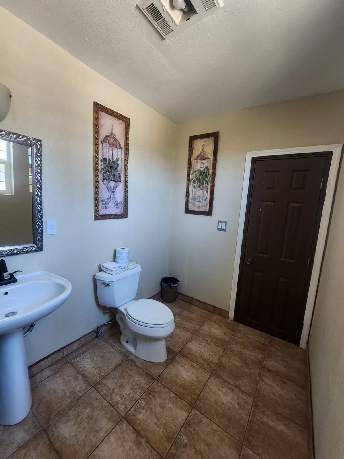 A bathroom with a sink, toilet, and two framed pictures on the wall.