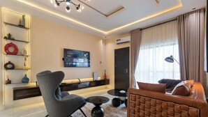 Una sala de estar moderna con un sofá, un sillón, televisión y objetos decorativos en estanterías.