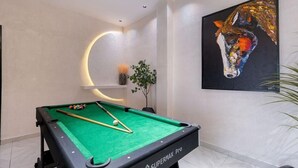 Una mesa de billar con la etiqueta Supermax Pro, un cuadro colgado en la pared de la cabeza de un caballo y una lámpara con forma circular.