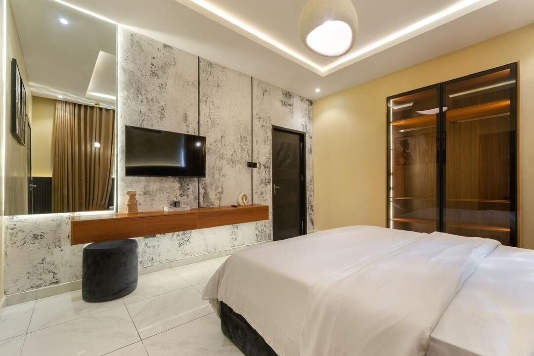 Una camera d'albergo moderna con un letto, una TV a parete, una toeletta in legno e uno specchio grande.