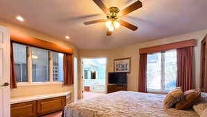 A bedroom with a large bed, a ceiling fan, a television, and a bathroom visible through an open door. - Los Indios sits on a secluded cove on Lake Thunderbird (Cherokee Village)