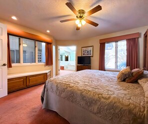 Ein Schlafzimmer mit einem großen Bett, einem Deckenventilator, einem Fernseher und einem durch eine offene Tür einsehbaren Badezimmer.