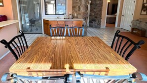 A dining area with a wooden table and chairs, a hanging rattan light fixture, a kitchen with a stone wall, and a view into another room. - Los Indios sits on a secluded cove on Lake Thunderbird (Cherokee Village)