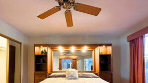 Une chambre à coucher avec un grand lit, un ventilateur de plafond, un miroir et des étagères intégrées.