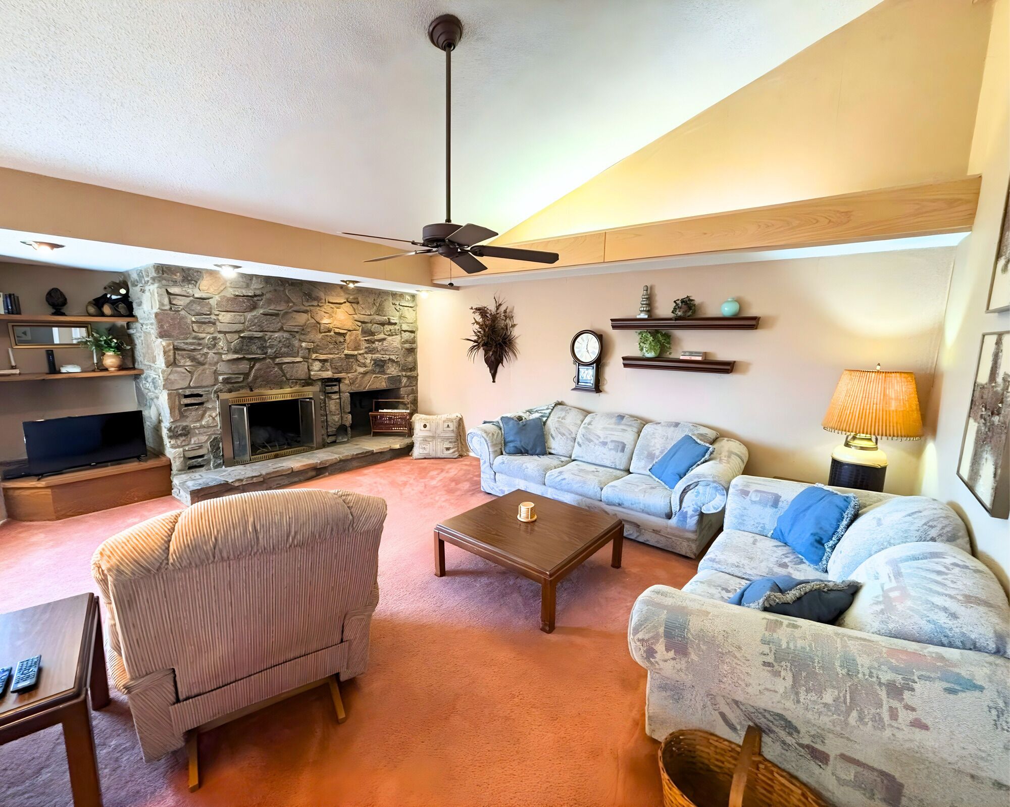 A living room with a stone fireplace, a ceiling fan, a television, a sofa, and a coffee table.