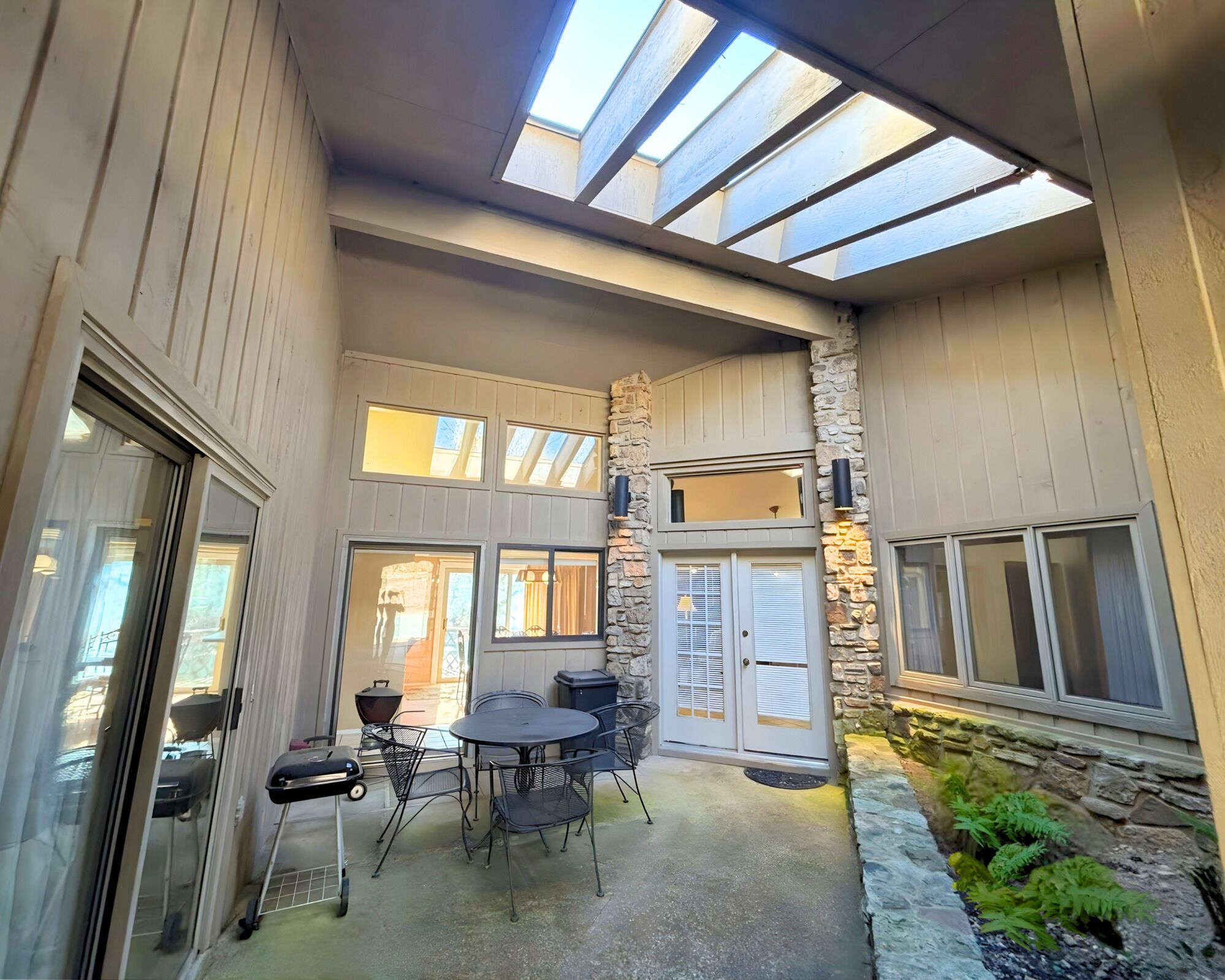 Ein überdachter Patio-Bereich mit Esstisch und Stühlen, einer Steinwand und Blick auf die umliegende Landschaft.