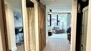 Ein Flur mit einer Schiebetür, eine Sitzecke mit Sofa und Sesseln sowie ein Blick auf Gebäude durch große Fenster.