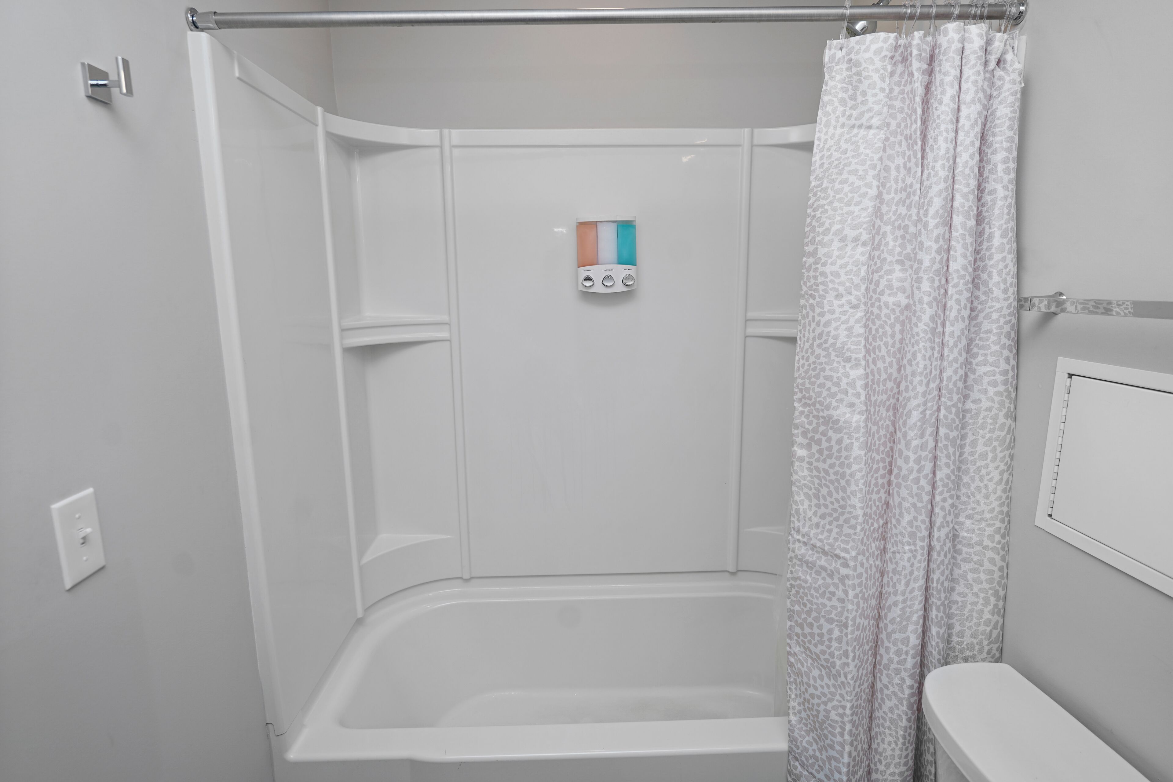 A shower with a control panel, a toilet, and a shower curtain.