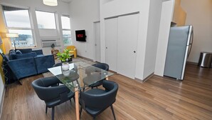 A modern living space with a glass dining table, black chairs, a blue sofa, and a white refrigerator.