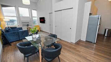 Un espacio habitable moderno con una mesa de comedor de vidrio, sillas negras, un sofá azul y un refrigerador blanco.