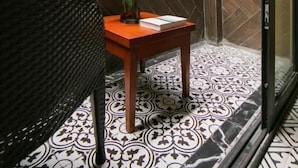 A room with a green artificial grass wall, a patterned floor, a wicker chair, a wooden table with a vase of flowers, and a glass door.
