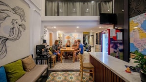 A hotel lobby with a dining area, a sofa, a TV, a map, and a wall with a fish mural.