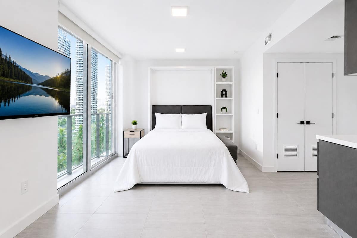 Quarto moderno com uma cama grande, televisão, mesa de cabeceira e vista para a cidade.