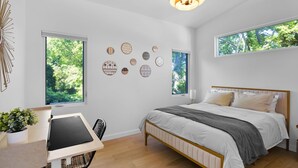 Un dormitorio con cama, escritorio, silla, planta en maceta y adornos en la pared.
