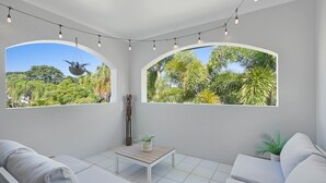 Ein Zimmer mit zwei großen Bogenfenstern, einer hängenden Leuchte, einem kleinen Tisch mit Pflanze und weißer Möbel.