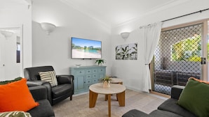 Ein Wohnzimmer mit Sofa, Couchtisch, Schrank, Fernseher und einer Schiebetür zu einem Außenbereich.