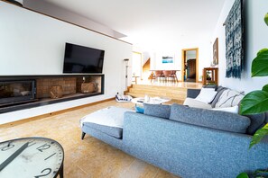 Ein Wohnzimmer mit einer Couch, einem Kamin, einem Fernseher und einem Essbereich im Hintergrund.