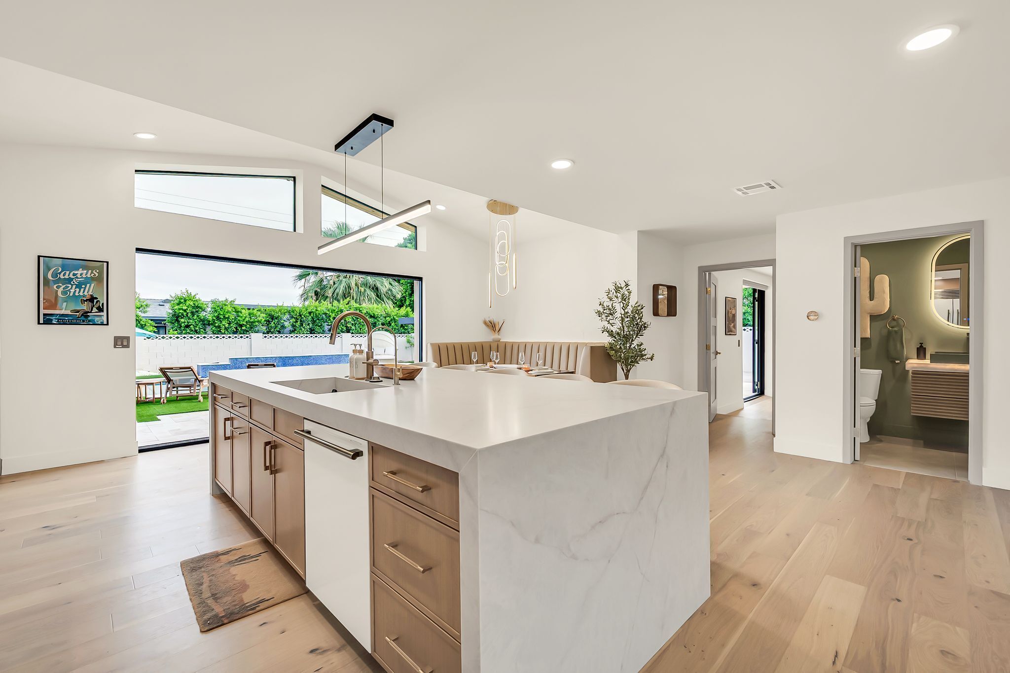 A modern kitchen with a large island, wooden cabinets, and a view of a garden.