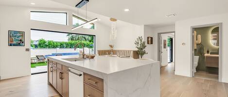 A modern kitchen with a large island, wooden cabinets, and a view of a garden.