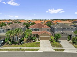 A residential neighborhood with houses featuring red-tiled roofs, a central driveway, and a street with a sidewalk. - Solterra Resort:Movie,Game & Lazy River near Disney! (Davenport)