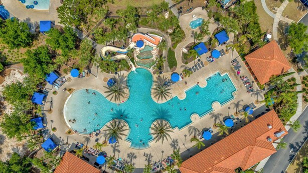 Ein Luftbild eines Resorts mit mehreren Schwimmbecken, Palmen und einer gewundenen Wasserrutsche.