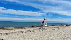 Ein Strand mit einem Rettungsschwimmerstuhl, sandigem Ufer und ruhiger See unter blauem Himmel.