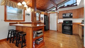 A kitchen with wooden cabinets, a central island with stools, a refrigerator, and a stove. - West Island Getaway - Unique 2 Bedroom Cottage (Fairhaven)