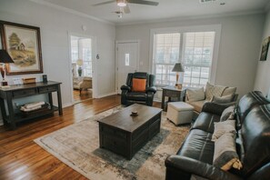 A living room with a dark wooden coffee table, a black leather sofa, and a beige armchair. There is a dark wooden console table with a lamp and a framed picture on the wall. - Executive Living 4BR 2BA in Beaumont (Beaumont)
