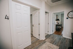 A hallway with white doors, a rug, and a lamp on a table. - Executive Living 4BR 2BA in Beaumont (Beaumont)