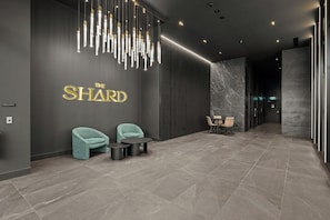 A modern lobby with a marble floor, two teal chairs, a small table, and a wall-mounted sign reading 'THE SHARD'. - 6min Walk to Westfield | Stylish 1BR Gem w/Parking (Phillip)