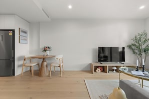 A modern living room with a dining area, a flat-screen TV, and a built-in kitchen unit. - 6min Walk to Westfield | Stylish 1BR Gem w/Parking (Phillip)