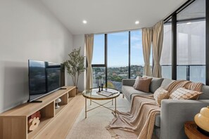 A modern living room with a flat-screen TV, a sofa, a coffee table, and a view of the city. - 6min Walk to Westfield | Stylish 1BR Gem w/Parking (Phillip)
