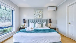A bedroom with a large bed, two bedside tables, a window, and an air conditioning unit.
