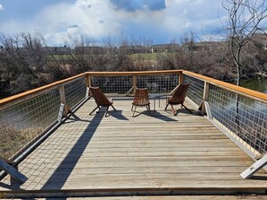 A wooden deck with a railing, two chairs, and a table.
