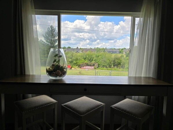 A kitchen counter with a fishbowl, three stools, and a window with a view of a residential area.